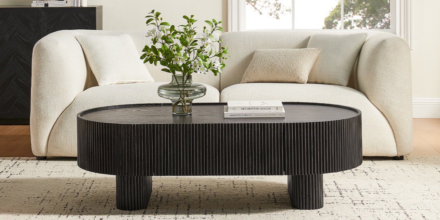 The Marisol 55 inch Oak Coffee Table, a circular black coffee table with detailed vertical fluting, is centered on a patterned beige rug.