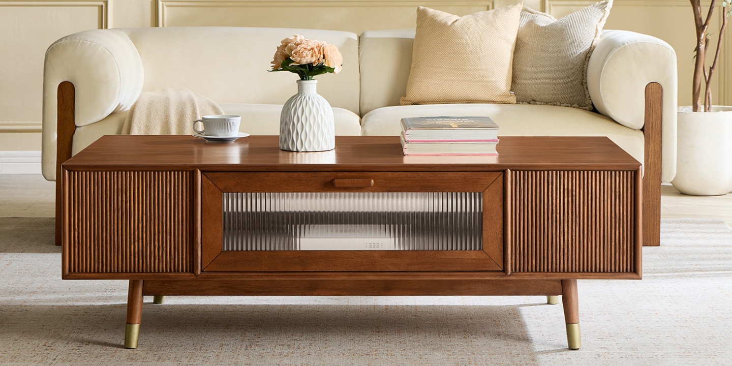Stavn 55" MCM Fluted Coffee Table with storage featuring a central glass-front drawer, fluted wood side panels, and gold metal-tipped legs in a refined living room interior
