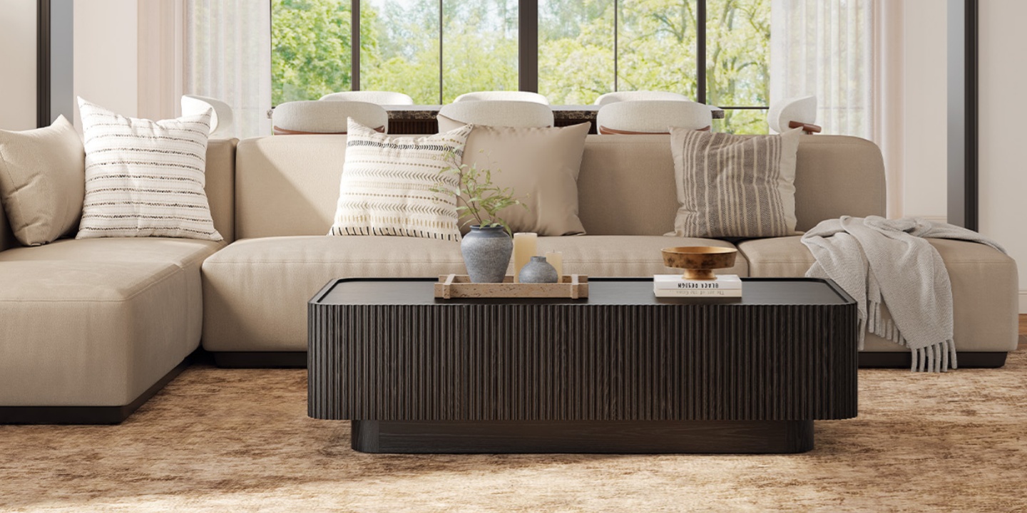 A modern, sunlit living room featuring a black coffee table with fluted details, a beige sectional sofa, and a vibrant garden view.