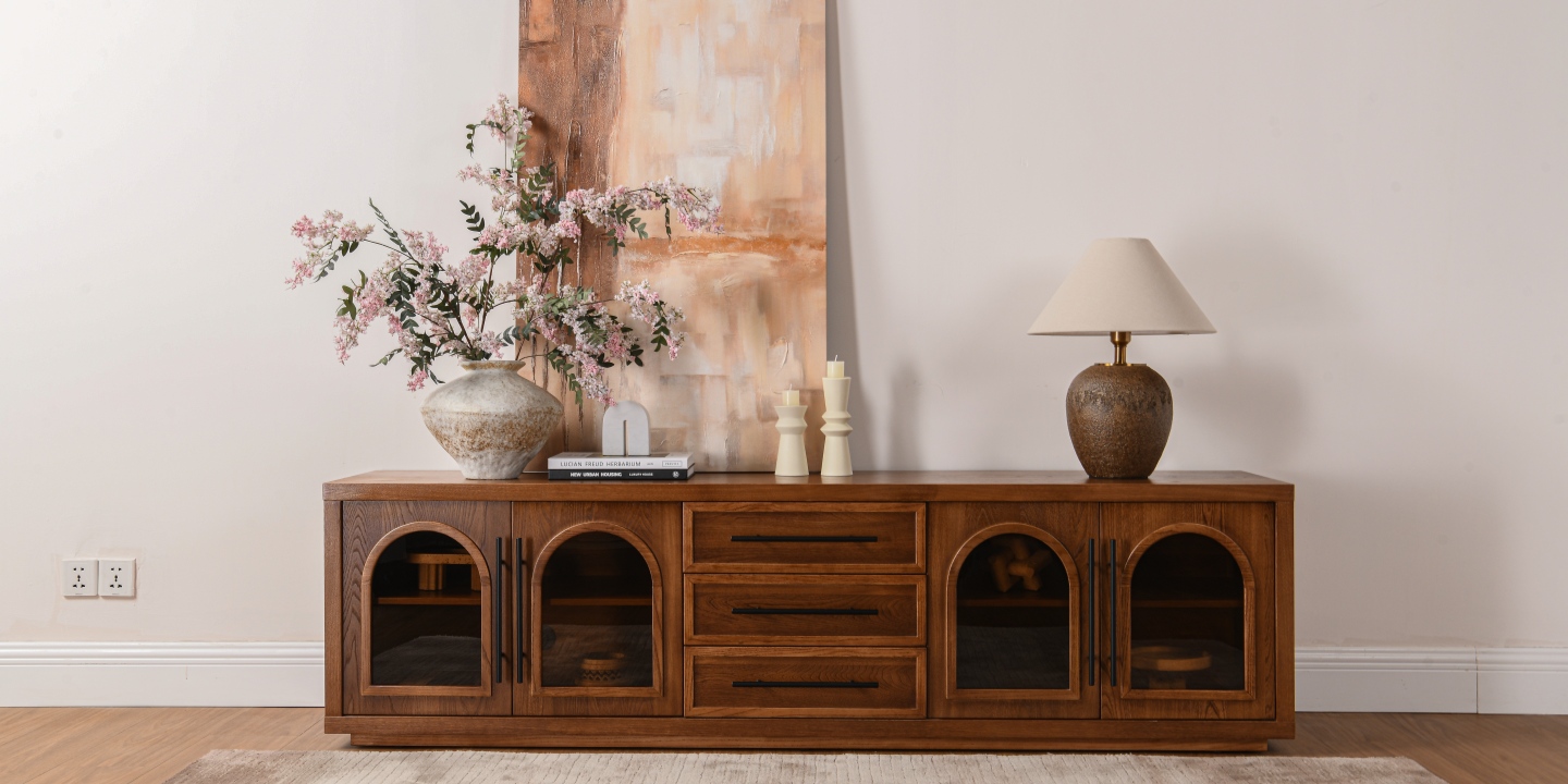 A Hernest 78 inch solid wood TV stand with arched doors styled with a floral vase, artwork, candle holders, and a table lamp. A Hernest 78 inch solid wood TV stand with arched doors styled with a floral vase, artwork, candle holders, and a table lamp.