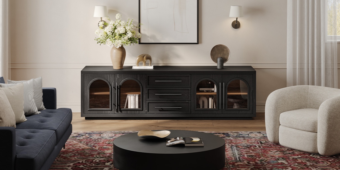 An 84-inch black media console with arched doors styled with a round coffee table, sofa, and armchair on a rug. An 84-inch black media console with arched doors styled with a round coffee table, sofa, and armchair on a rug.