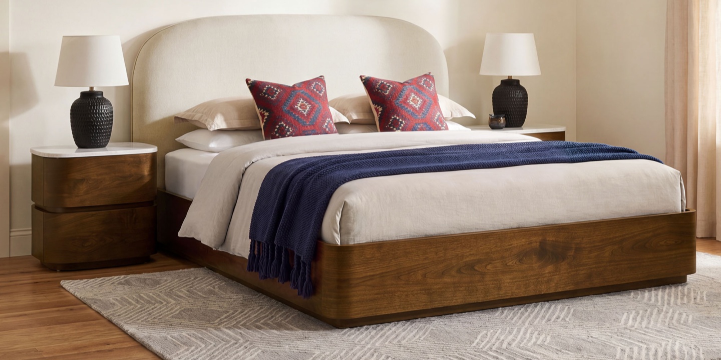 A wood bed frame with a cream upholstered headboard is styled with a blue throw blanket and matching nightstands. A wood bed frame with a cream upholstered headboard is styled with a blue throw blanket and matching nightstands.