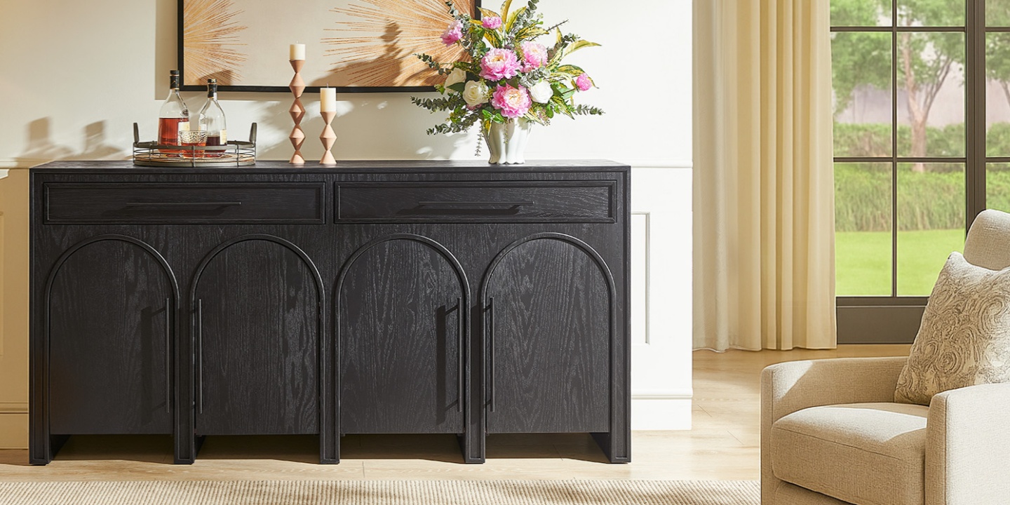 A 72 inch dark wood sideboard with arched door details. Styled with a drink tray, candles, and pink flowers. A 72 inch dark wood sideboard with arched door details. Styled with a drink tray, candles, and pink flowers.