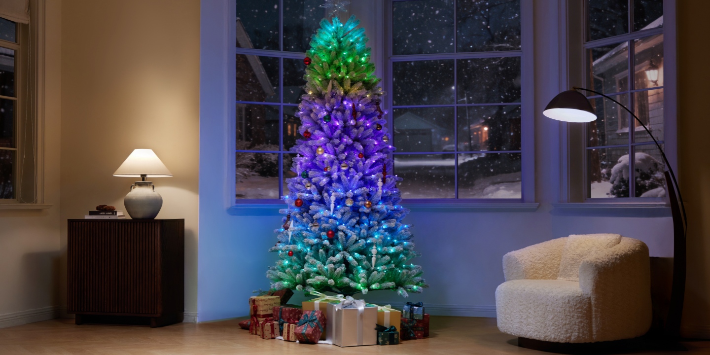 A vibrant, color-changing Christmas tree stands surrounded by wrapped gifts in a cozy living room with snowy windows.