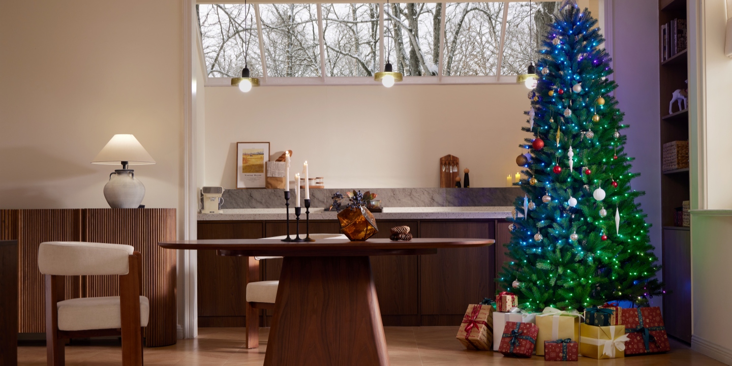 Modern dining room featuring the Hernest CastGlow artificial Christmas tree glowing with colorful lights and wrapped gifts underneath. Modern dining room featuring the Hernest CastGlow artificial Christmas tree glowing with colorful lights and wrapped gifts underneath.