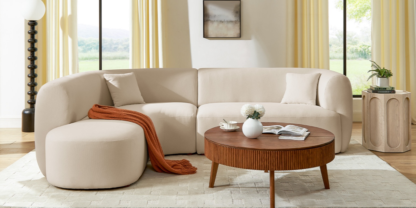 A beige curved sectional sofa with a chaise features soft cotton fabric, an orange throw blanket, and a round wooden table. A beige curved sectional sofa with a chaise features soft cotton fabric, an orange throw blanket, and a round wooden table.