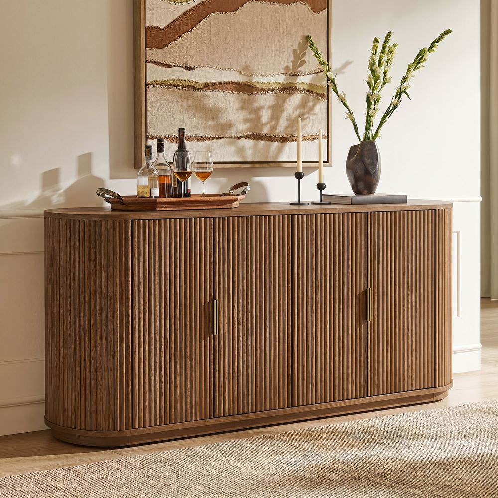 Styled view of the Hernest Rolf 63 inch Oak Sideboard in an elegant room, featuring a fluted wood design and styled with modern lamps and a vase.