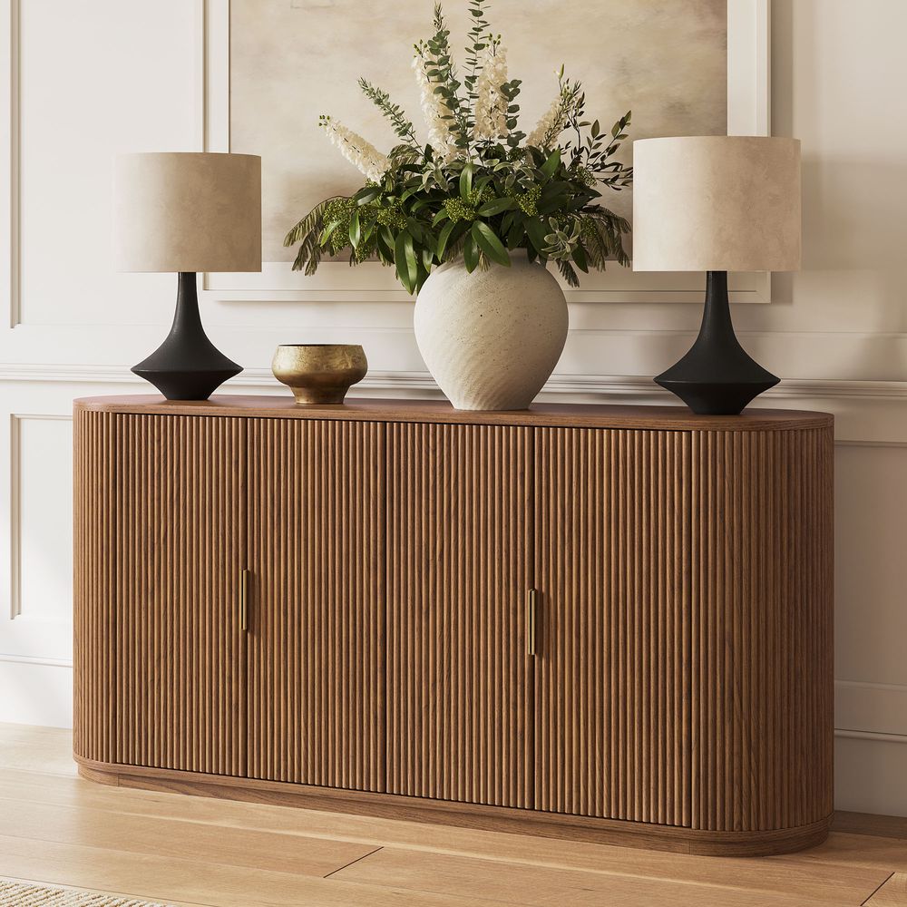 Styled view of the Hernest Rolf 63 inch Oak Sideboard in an elegant room, featuring a fluted wood design and styled with modern lamps and a vase.