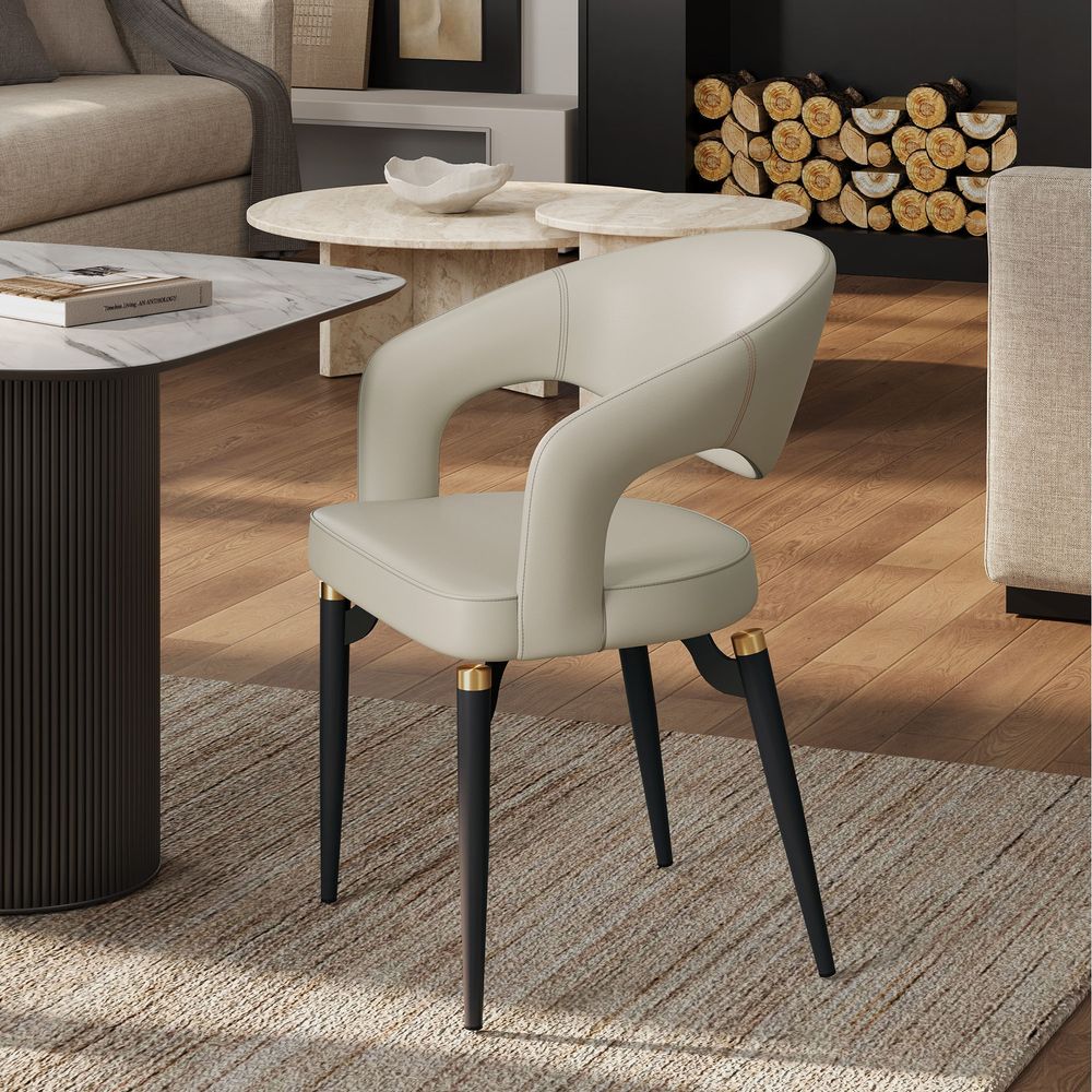 Side view of the beige Hernest Liliana Armrest Leather Dining Chair, featuring a curved cutout back and legs with elegant golden metal accents.