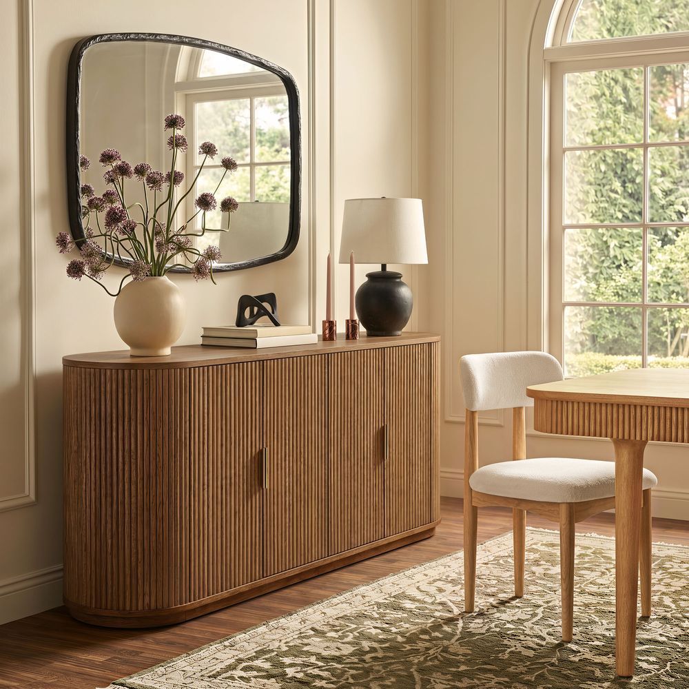 Styled view of the Hernest Rolf 63 inch Oak Sideboard in an elegant room, featuring a fluted wood design and styled with modern lamps and a vase.
