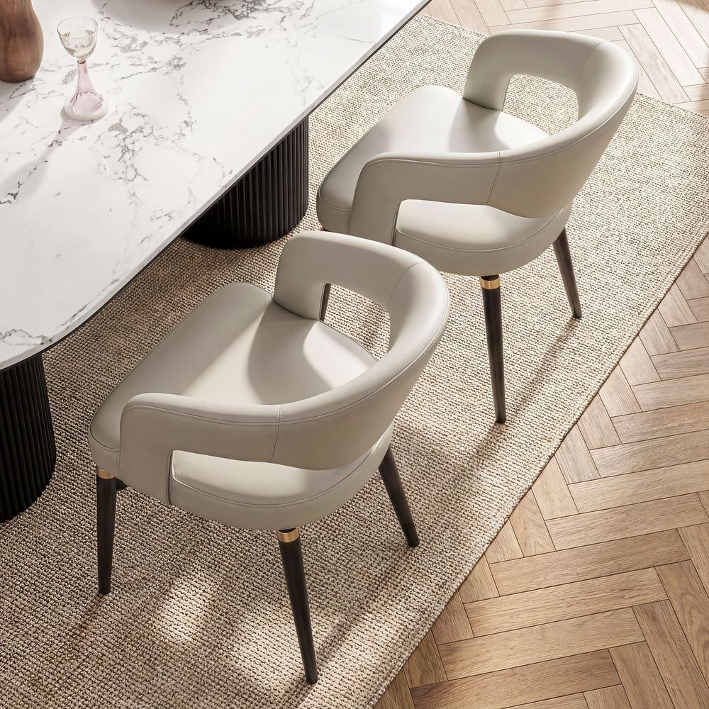 Orange DinTwo modern beige Hernest Liliana Armrest Leather Dining Chairs with curved backs and gold-accented black legs, shown together.ing Chair Set
