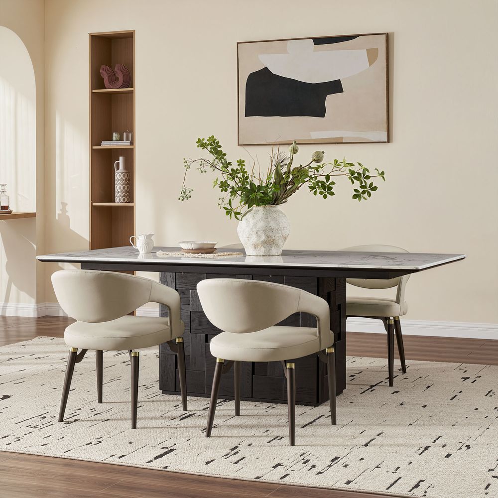 A modern beige Hernest Liliana Armrest Leather Dining Chair featuring gold-accented black legs, positioned beside a dining table.