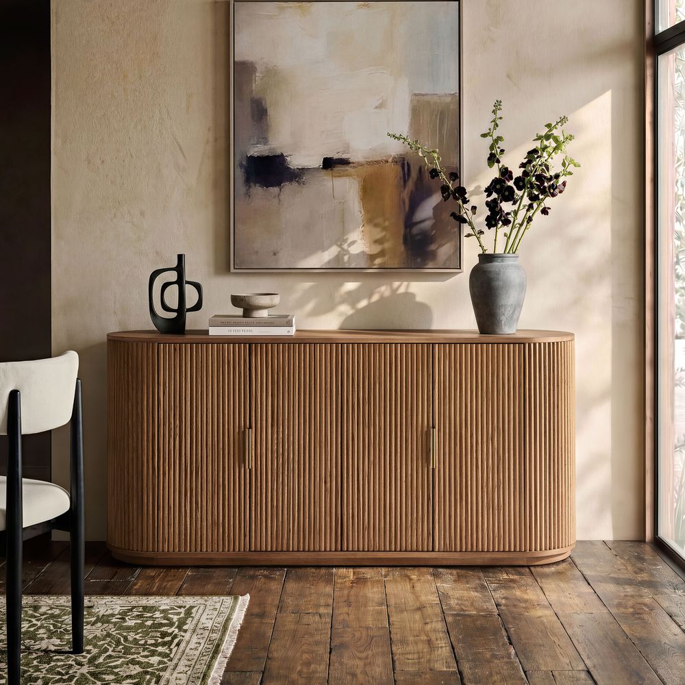 Styled view of the Hernest Rolf 63 inch Oak Sideboard in an elegant room, featuring a fluted wood design and styled with modern lamps and a vase.