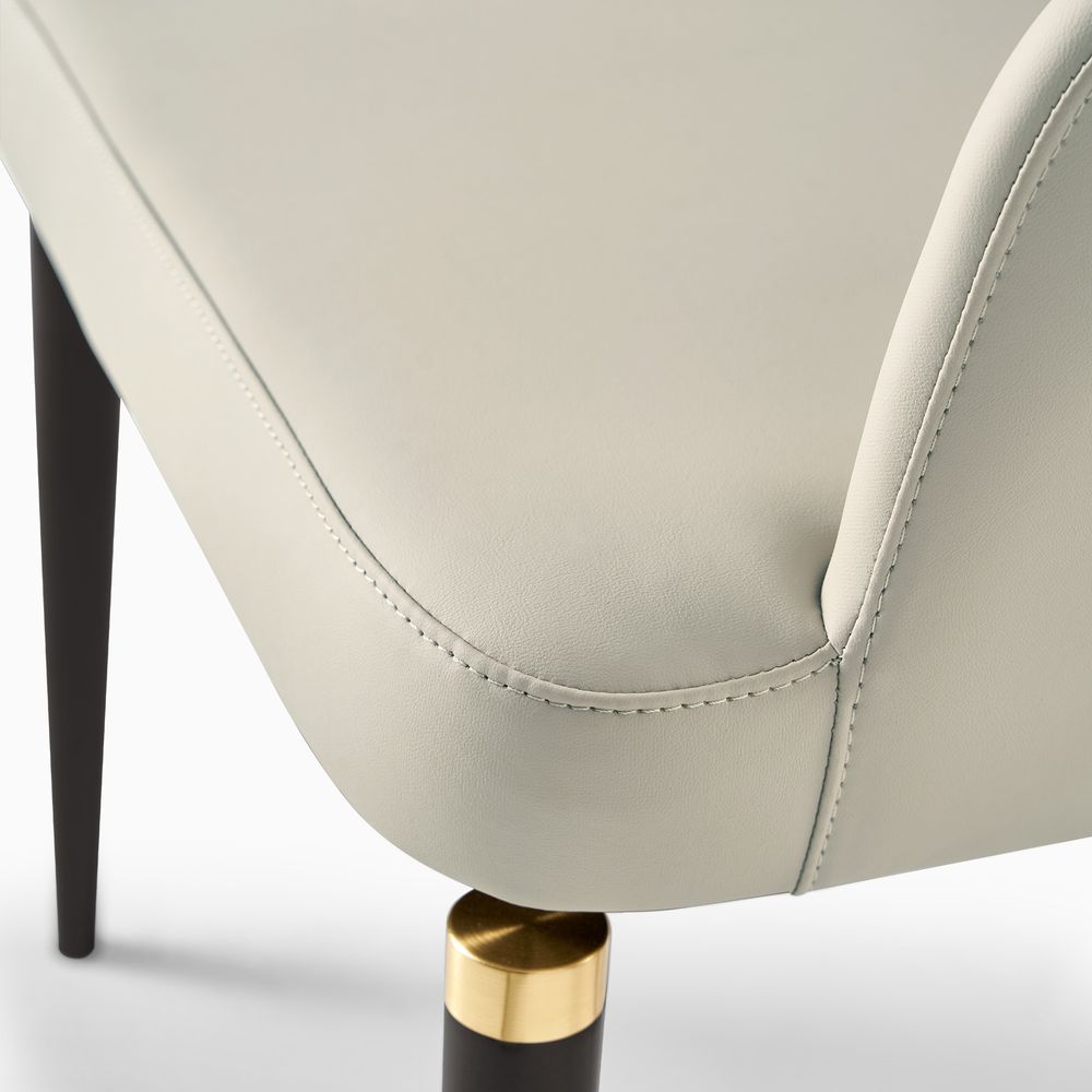 Close-up of the Hernest Liliana Armrest Leather Dining Chair, featuring the golden metal accent on the black leg and PU leather seat.
