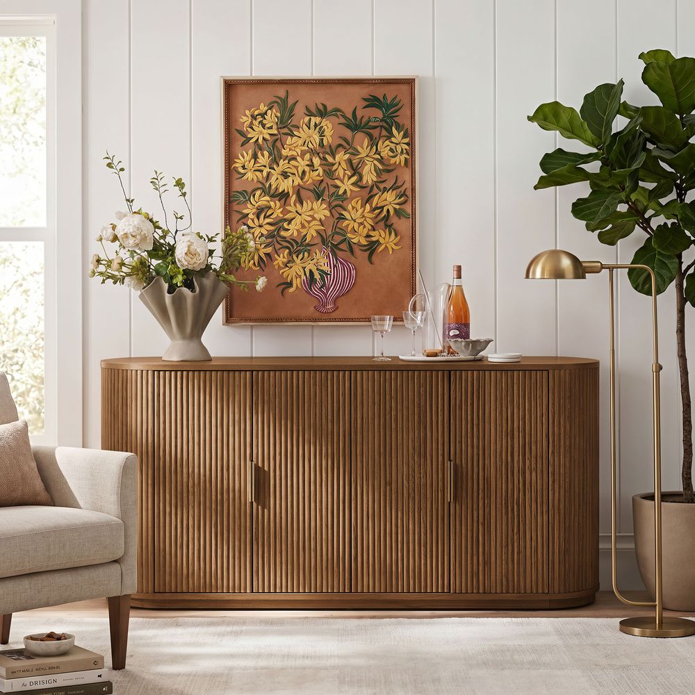 Styled view of the Hernest Rolf 63 inch Oak Sideboard in an elegant room, featuring a fluted wood design and styled with modern lamps and a vase.