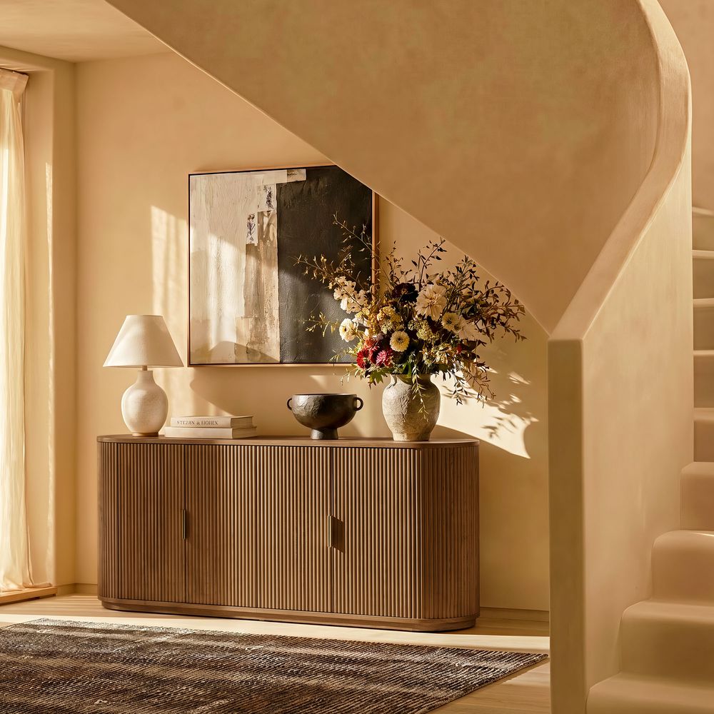 Styled view of the Hernest Rolf 63 inch Oak Sideboard in an elegant room, featuring a fluted wood design and styled with modern lamps and a vase.