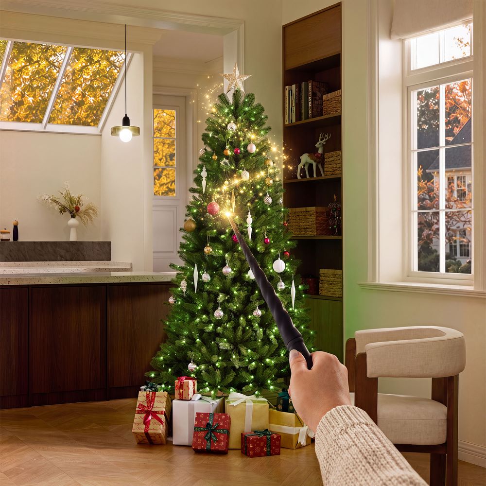 POV shot of a hand holding a wand casting a spell on a decorated CastGlow 6.5ft slim green Christmas tree with warm lights and ornaments.