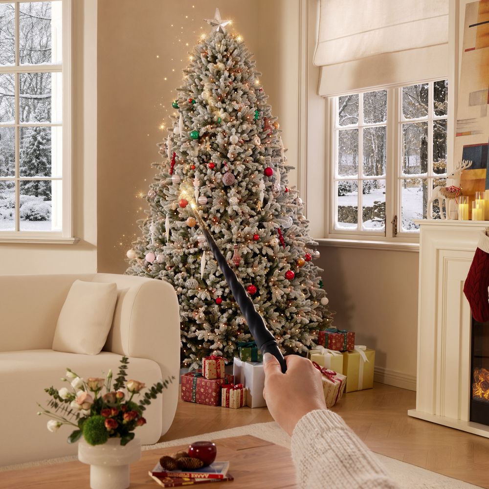 Person using a magic wand to control the lights on a fully decorated flocked artificial Christmas tree.