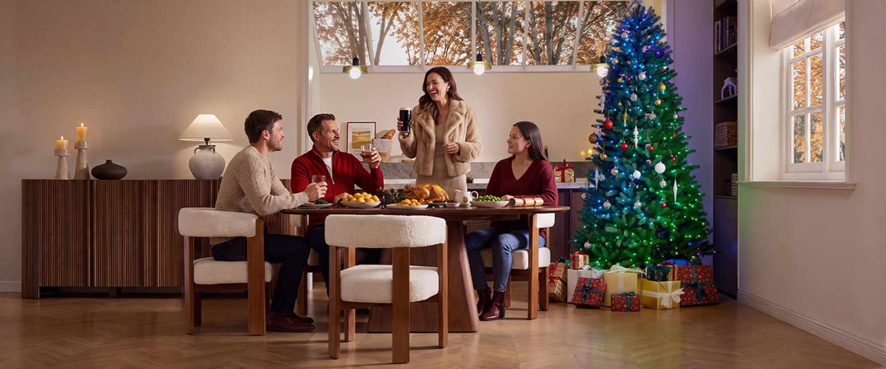 Family enjoying a cozy holiday dinner with the CastGlow 7.5 ft pre-lit slim green Christmas tree glowing nearby.